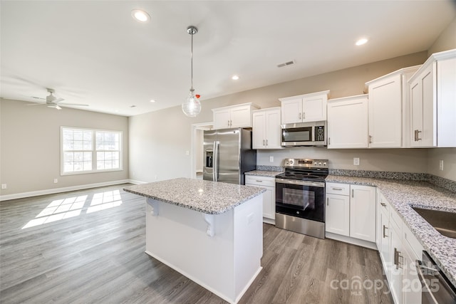 kitchen with pendant lighting, appliances with stainless steel finishes, white cabinetry, light stone countertops, and light wood-type flooring