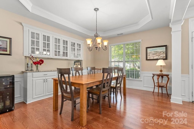 dining area featuring crown molding, light wood-type flooring, a chandelier, a tray ceiling, and decorative columns