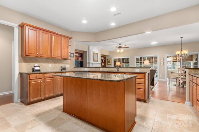 kitchen featuring dark stone countertops, ceiling fan with notable chandelier, kitchen peninsula, a kitchen island, and decorative backsplash