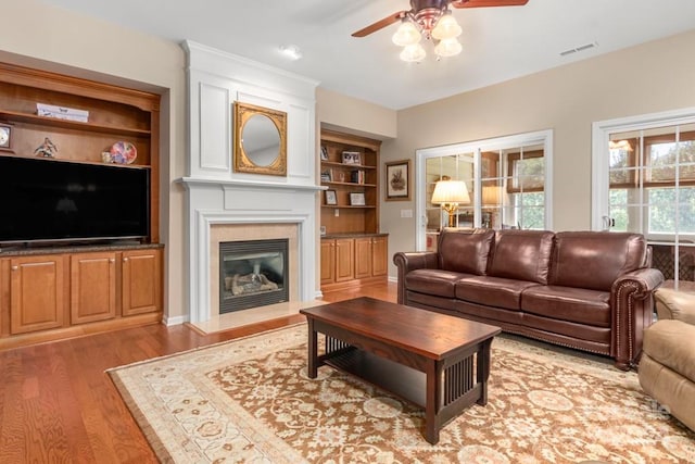 living room featuring built in shelves, ceiling fan, and light hardwood / wood-style floors