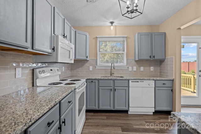 kitchen with white appliances, dark wood-style flooring, light stone countertops, gray cabinetry, and a sink