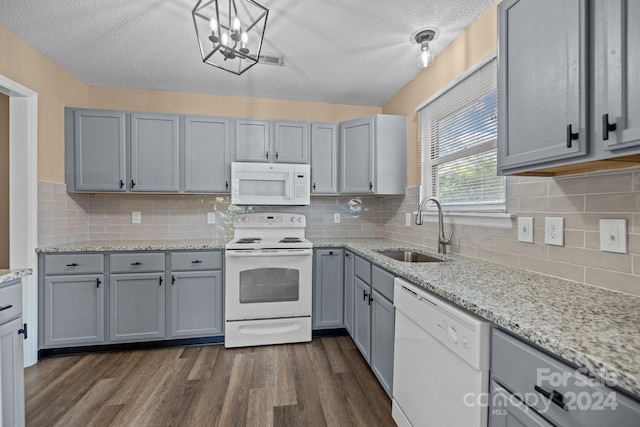 kitchen with white appliances, dark wood-style floors, light stone countertops, gray cabinetry, and a sink