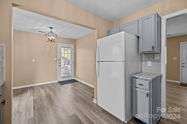 kitchen featuring gray cabinets, wood finished floors, freestanding refrigerator, a textured ceiling, and light stone countertops