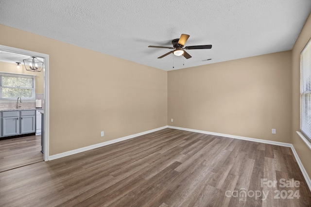 unfurnished room featuring a textured ceiling, ceiling fan with notable chandelier, wood finished floors, a sink, and baseboards