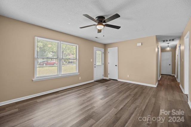 unfurnished room with baseboards, visible vents, a ceiling fan, dark wood-type flooring, and a textured ceiling