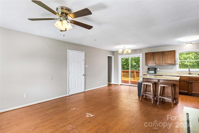 kitchen with ceiling fan with notable chandelier, a textured ceiling, a kitchen breakfast bar, and dark hardwood / wood-style floors