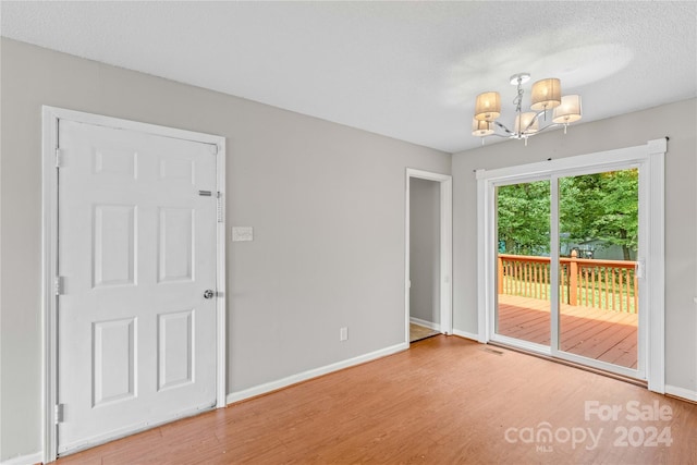 unfurnished room featuring light wood-type flooring, an inviting chandelier, and a textured ceiling