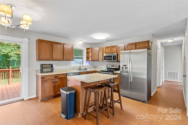 kitchen featuring light hardwood / wood-style flooring, a kitchen island, sink, hanging light fixtures, and appliances with stainless steel finishes