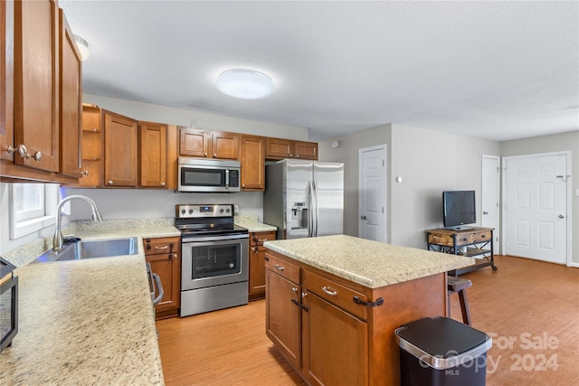 kitchen featuring a textured ceiling, appliances with stainless steel finishes, light hardwood / wood-style floors, a center island, and sink