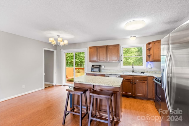 kitchen featuring light wood-type flooring, a notable chandelier, a kitchen island, sink, and appliances with stainless steel finishes