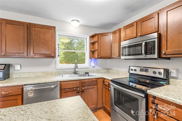 kitchen featuring a textured ceiling, stainless steel appliances, sink, light stone counters, and light wood-type flooring