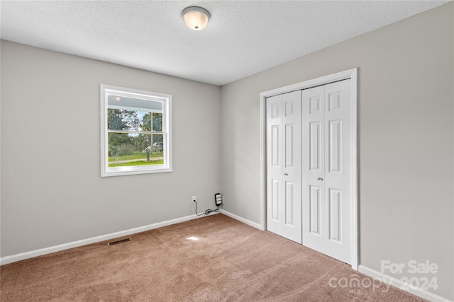 unfurnished bedroom featuring carpet flooring, a textured ceiling, and a closet