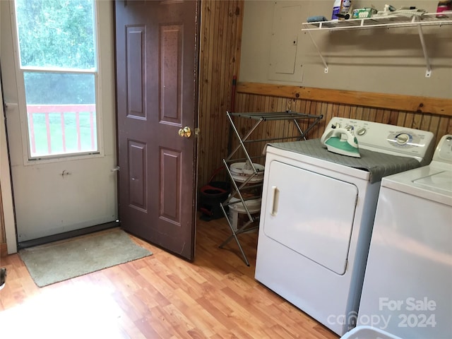 laundry area featuring light wood-type flooring, wood walls, and washer and clothes dryer