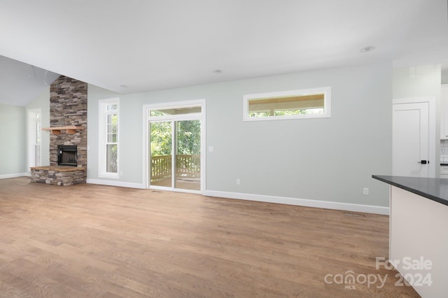 unfurnished living room featuring a stone fireplace, light wood-type flooring, and vaulted ceiling