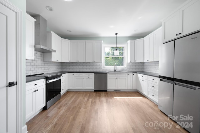 kitchen featuring stainless steel appliances, wall chimney range hood, light hardwood / wood-style flooring, and pendant lighting