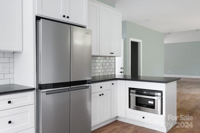 kitchen featuring kitchen peninsula, white cabinets, backsplash, appliances with stainless steel finishes, and dark hardwood / wood-style floors