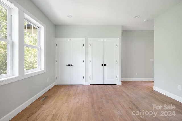 unfurnished bedroom with multiple closets, multiple windows, and light wood-type flooring