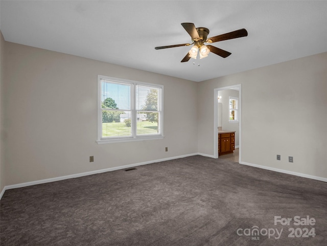 unfurnished bedroom with connected bathroom, dark colored carpet, and ceiling fan