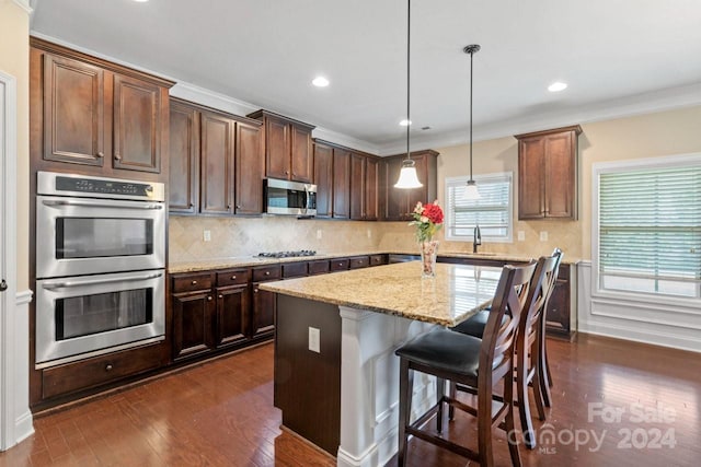 kitchen with light stone counters, dark hardwood / wood-style flooring, stainless steel appliances, a center island, and decorative light fixtures