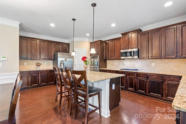 kitchen with pendant lighting, dark hardwood / wood-style floors, a kitchen island, appliances with stainless steel finishes, and light stone countertops