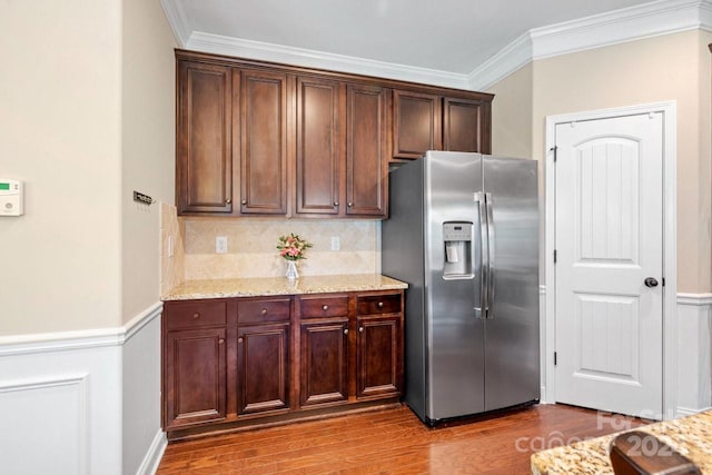 kitchen with wood-type flooring, light stone counters, stainless steel fridge with ice dispenser, backsplash, and crown molding