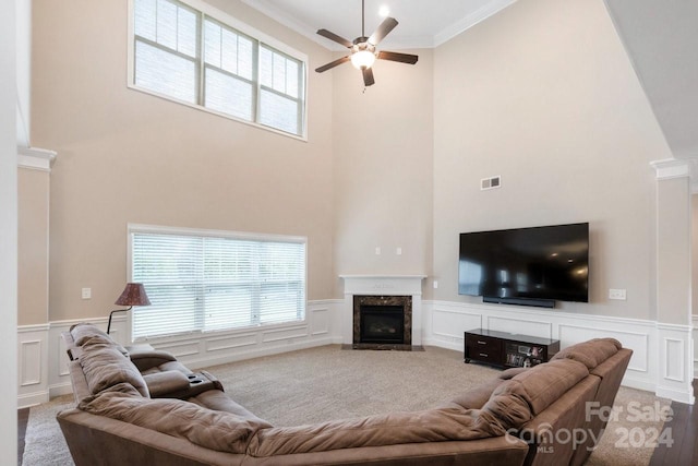 living room with a premium fireplace, a towering ceiling, hardwood / wood-style floors, ornamental molding, and ceiling fan