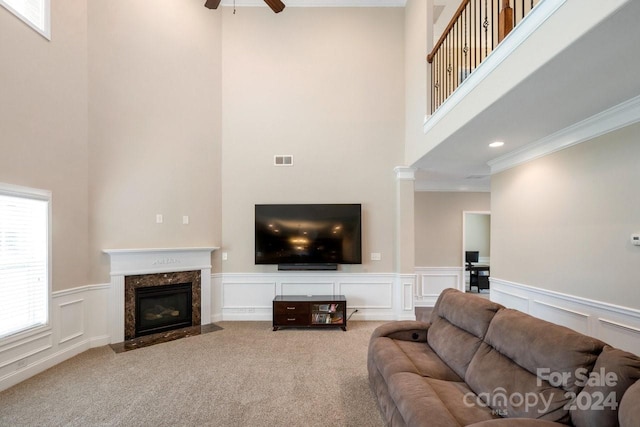 carpeted living room with crown molding, a towering ceiling, ceiling fan, and a premium fireplace