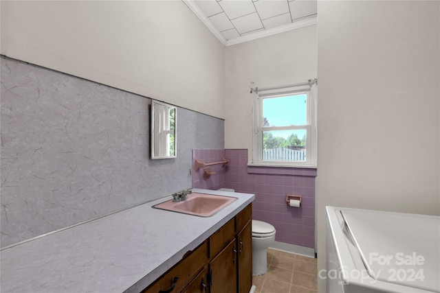 bathroom with toilet, tile patterned floors, ornamental molding, vanity, and tile walls