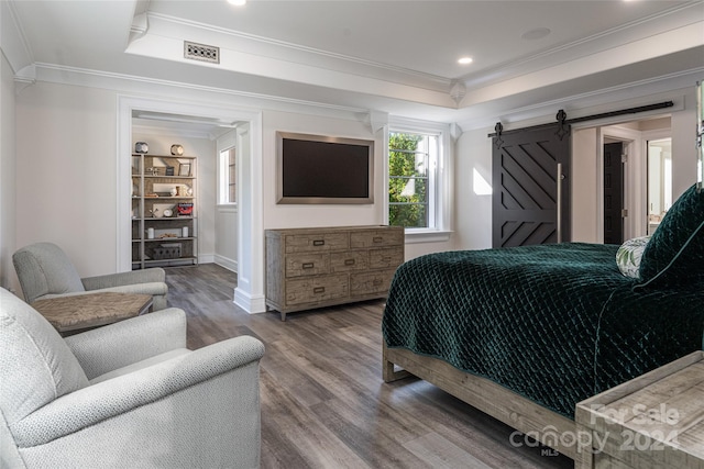 bedroom with a barn door, a tray ceiling, wood-type flooring, and crown molding