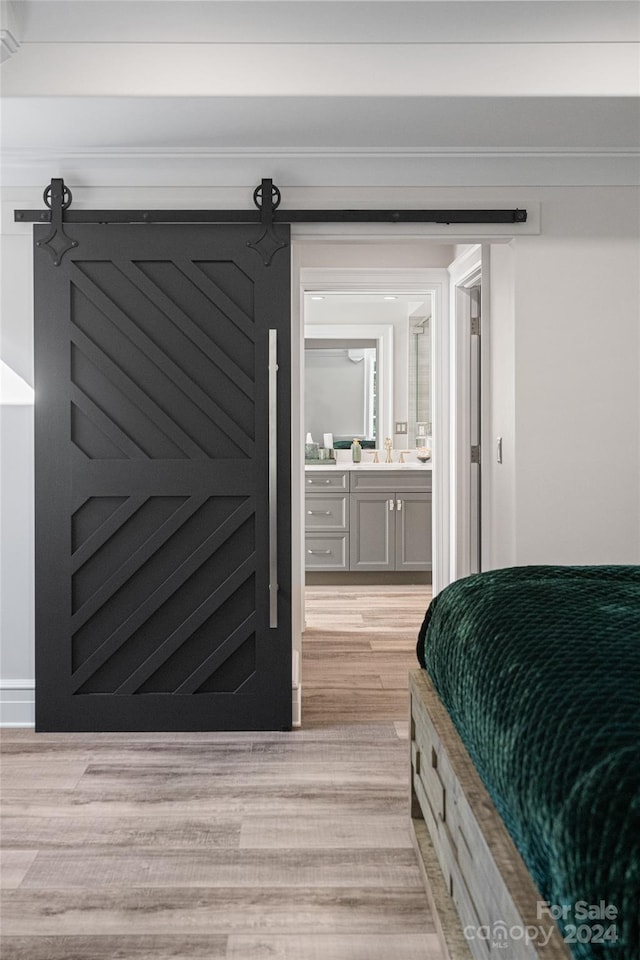 bedroom with a barn door, ensuite bath, sink, and light hardwood / wood-style flooring