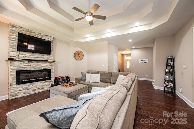 living room with a raised ceiling, a fireplace, ceiling fan, and dark wood-type flooring