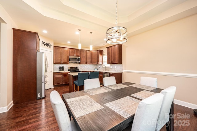 dining area featuring sink, an inviting chandelier, a tray ceiling, and dark wood-type flooring