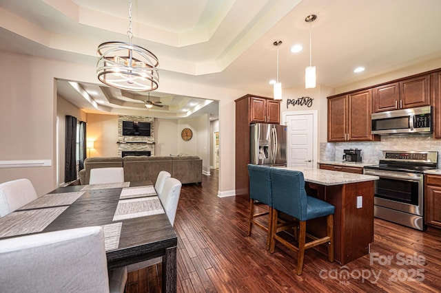 kitchen with stainless steel appliances, light stone counters, a raised ceiling, a kitchen bar, and pendant lighting