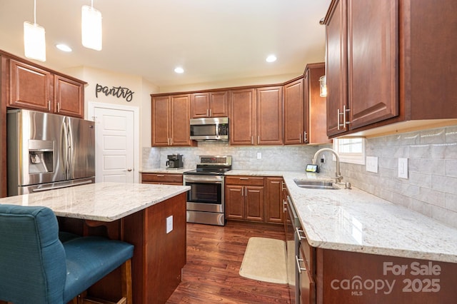 kitchen with light stone counters, hanging light fixtures, a kitchen island, appliances with stainless steel finishes, and sink