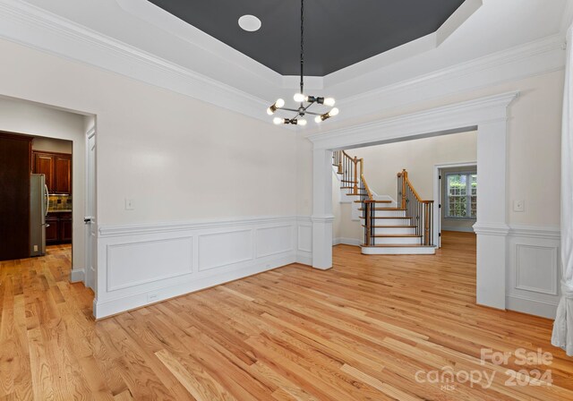 spare room with ornamental molding, light hardwood / wood-style floors, a tray ceiling, and a notable chandelier