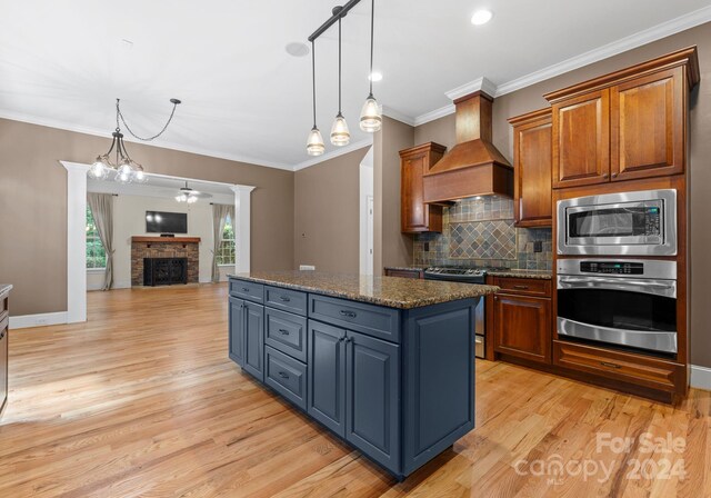 kitchen featuring light wood-type flooring, custom range hood, stainless steel appliances, decorative light fixtures, and a center island