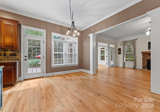 unfurnished dining area featuring light wood-type flooring, an inviting chandelier, a stone fireplace, and crown molding