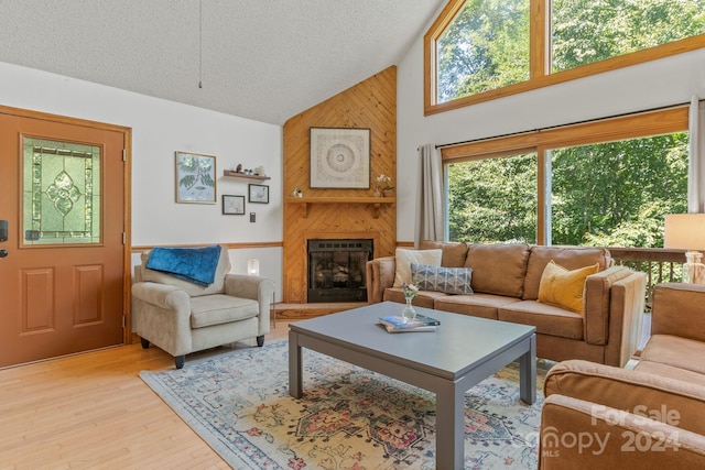 living room with a fireplace, high vaulted ceiling, a textured ceiling, light hardwood / wood-style flooring, and wood walls