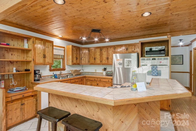 kitchen with a kitchen bar, kitchen peninsula, appliances with stainless steel finishes, and tile countertops