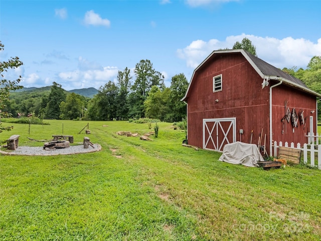 view of yard with a fire pit, a barn, a garage, fence, and an outbuilding