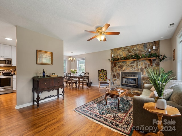 living room with visible vents, baseboards, light wood-type flooring, a textured ceiling, and ceiling fan with notable chandelier