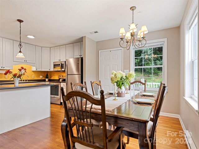 dining area with light wood finished floors, a notable chandelier, baseboards, and visible vents