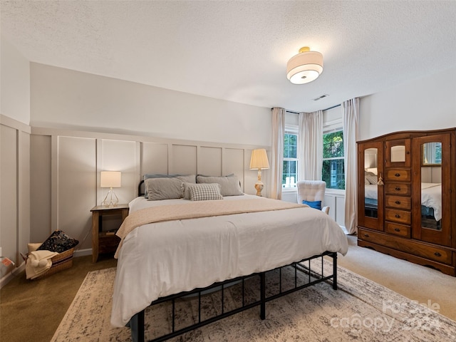 bedroom with a decorative wall, carpet, a textured ceiling, visible vents, and a wainscoted wall