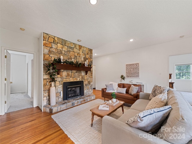 living area featuring recessed lighting, light wood-style floors, a stone fireplace, and a textured ceiling