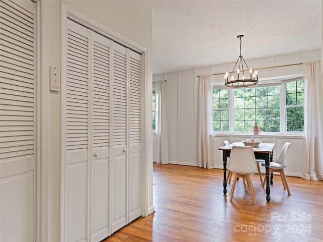 dining area with light wood-style flooring, a textured ceiling, and an inviting chandelier