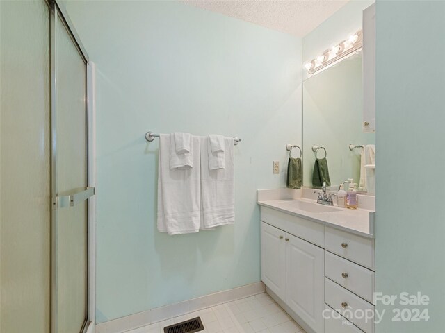 bathroom with a textured ceiling, a shower with shower door, vanity, visible vents, and baseboards