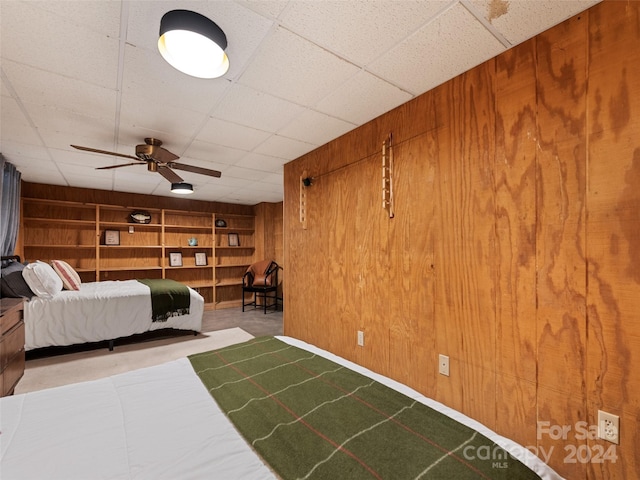 unfurnished bedroom with wooden walls, a drop ceiling, and ceiling fan