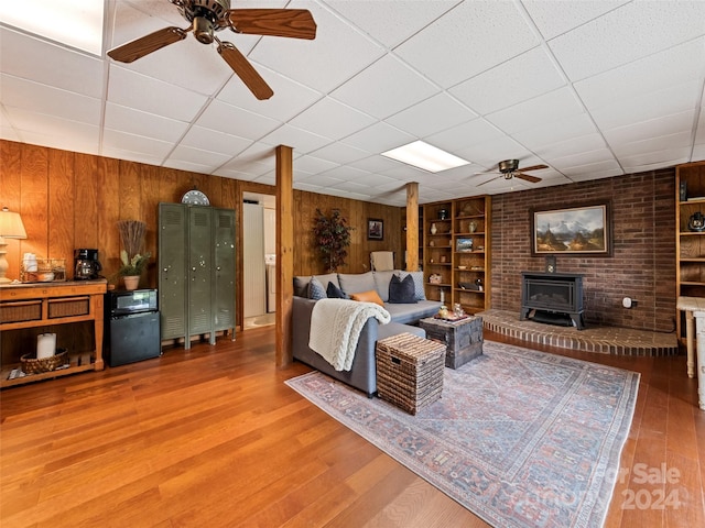 living area with a wood stove, a ceiling fan, wood finished floors, wood walls, and built in shelves