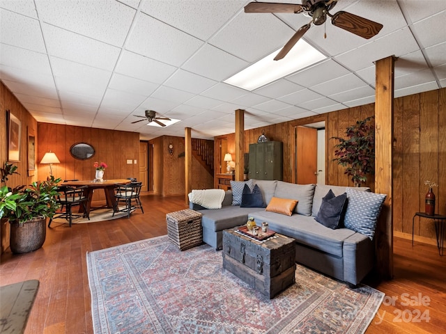 living area featuring wood walls, stairs, wood-type flooring, and ceiling fan