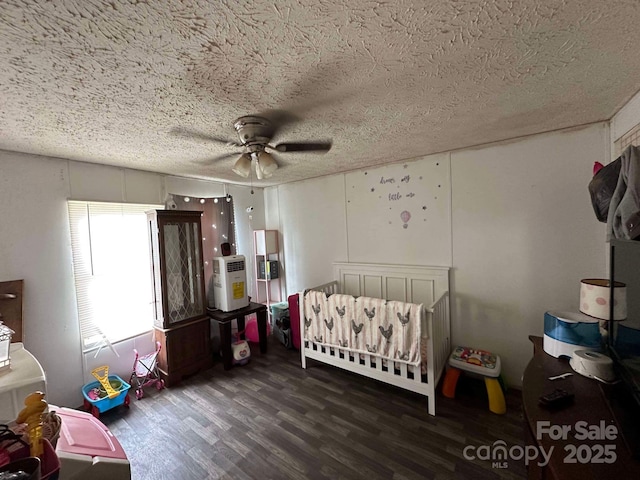 bedroom featuring ceiling fan, a nursery area, dark hardwood / wood-style floors, and a textured ceiling